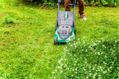Bahçede çim biçme makinesiyle çim biçen bir adam. Bahçe işleri kırsal yaşam tarzı. Güneş ışığında taze yeşil çimlerin manzarası baharda ya da yaz mevsiminde bahçe manzarası
