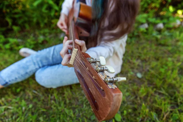 Closeup of woman hands playing acoustic guitar on park or garden background. Teen girl learning to play song and writing music. Hobby, lifestyle, relax, Instrument, leisure, education concept