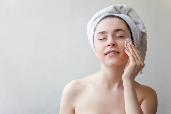 一个微笑的黑发妇女在毛巾在头与柔软健康的皮肤去除化妆与棉垫查出在白色背景的美丽的画像 护肤性清洁水疗放松的概念 — 图库照片