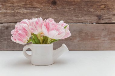 Bahar tebrik kartı. Taze hafif pastel pembe Lale buketi küçük oyuncak sulama olabilir vazo rustik ahşap arka plan üzerinde çiçekler. Mutlu tatil anne gün Sevgililer günü kavramı. Düz yatıyordu üstten görünüm kopya alanı