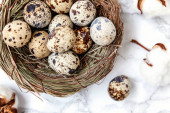 Velikonoční dekorace s vejcem v hnízdo a bavlněné na bílém mramorovém pozadí. Velikonoční koncept. Prostor, kopie ploché laický pohled shora. Jaro přání