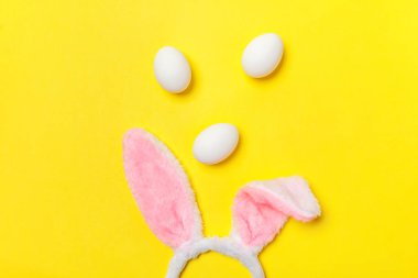 Mutlu Paskalya kavramı. Tatil için hazırlık. Dekoratif beyaz yumurta ve tüylü kostüm oyuncak trendy sarı arka plan üzerinde izole bunny kulaklar. Üstten görünüm kopya alanı basit minimalizm düz yatıyordu