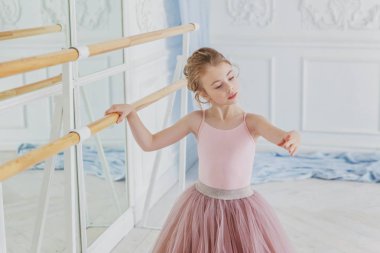 Dans sınıfındaki genç klasik balerin kız. Güzel, zarif balerin, bale pozisyonu pembe etekli, beyaz ışıklı salonda büyük aynanın yanında.