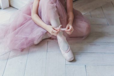 Pembe etekli balerin elleri beyaz ışıklı salonda sivri uçlu ayakkabılar giyer. Dans sınıfındaki genç klasik balerin kız.