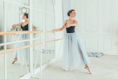 Genç Klasik Bale dansçısı kadın dans dersi. Güzel zarif balerin pratik bale pozisyonlar yakınındaki beyaz ışık salonda büyük ayna mavi tutu etekle