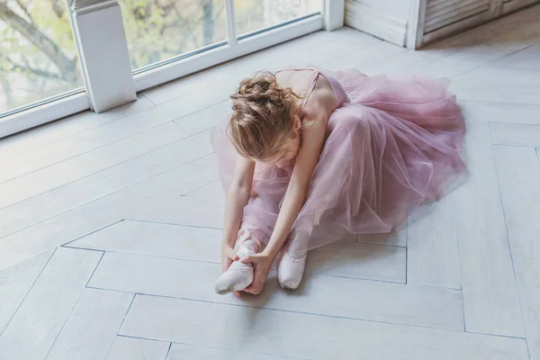 Young classical ballet dancer girl in dance class. Beautiful graceful ballerina practice ballet positions in pink tutu skirt in white light hall