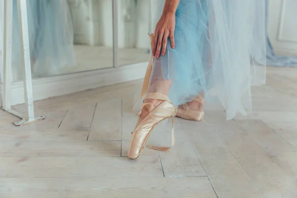 白い光ホールで足のポワント シューズに青いチュチュ スカートのバレリーナの手を置きます ダンス クラスの若いバレエ ダンサー女 — ストック写真