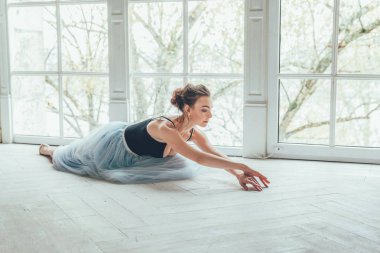 Genç Klasik Bale dansçısı kadın dans dersi. Mavi tutu etek beyaz ışık salonda büyük pencere yakınındaki güzel zarif balerin pratik bale pozisyonlar