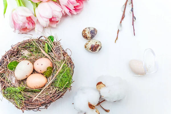 Bahar tebrik kartı. Paskalya yumurtaları içinde iç içe pamuk söğüt dalı ve pembe taze Lale çiçek buketi beyaz rustik ahşap zemin üzerinde. Paskalya kavramı. Düz yatıyordu üstten görünüm kopya alanı. Bahar çiçekler