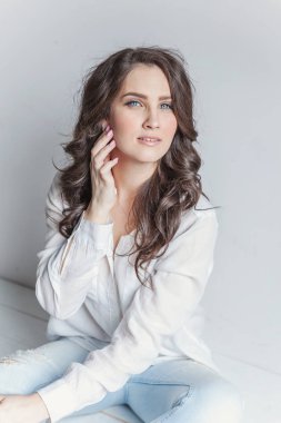 Mutlu genç kız gülümsüyor. Beyaz gömlek beyaz duvara parlak oda katta oturan genç mutlu pozitif kadın. Avrupa kadın. Olumlu insan duygu yüz ifadesi beden dili