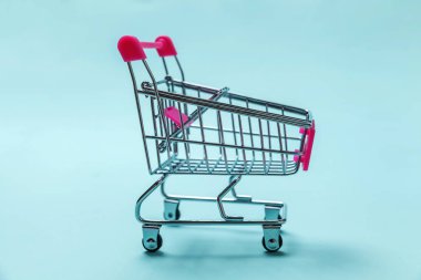 Satılık alışveriş merkezi Pazar Dükkanı tüketici kavramı satın. Küçük süpermarket bakkal itme izole mavi pastel renkli kağıt trendy arka plan üzerinde tekerlekli için alışveriş oyuncak sepeti. Kopya alanı