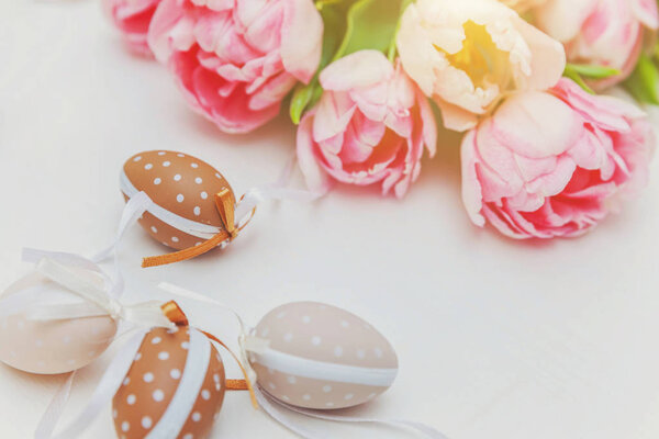 Easter eggs with moss cotton and pink fresh tulip bouquet on rustic white wooden background