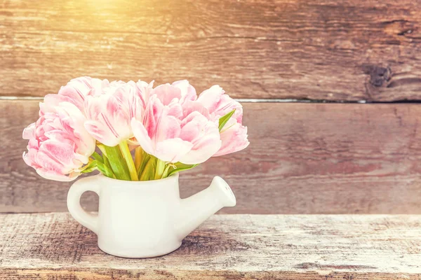 Buquê de flores de tulipas rosa frescas e pequena rega de brinquedos pode vaso no fundo de madeira rústica — Fotografia de Stock