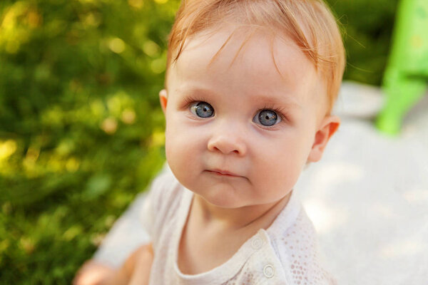 Sweet happy little baby girl sitting on grass in park, garden, meadow