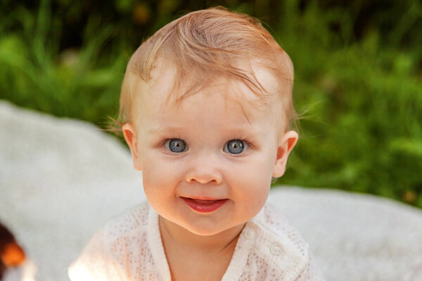 Sweet happy little baby girl sitting on grass in park, garden, meadow