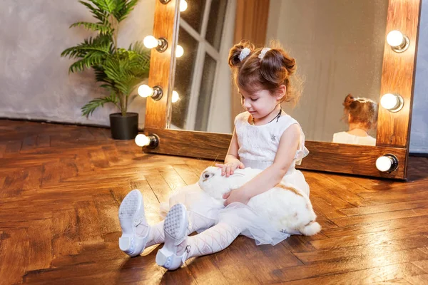 Menina sentada no chão e brincando com coelho branco no quarto moderno sobre espelho — Fotografia de Stock