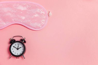 Uyku maskesi ve pembe bir arka plan üzerinde çalar saat
