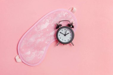 Uyku maskesi ve pembe bir arka plan üzerinde çalar saat