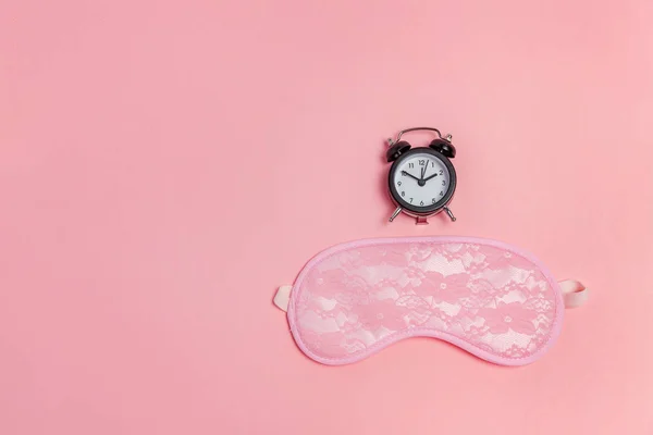 Sleeping mask and alarm clock on pink background