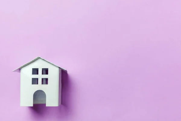 Miniaturowe zabawki biały dom na fioletowy fiołek pastelowe tło — Zdjęcie stockowe