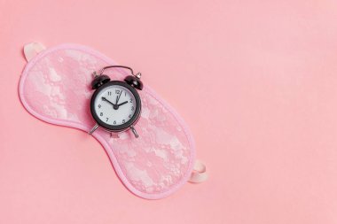 Uyku maskesi ve pembe bir arka plan üzerinde çalar saat