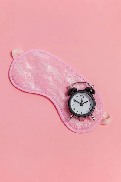 在粉红色背景的睡眠面罩和闹钟 — 图库照片