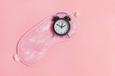 Uyku maskesi ve pembe bir arka plan üzerinde çalar saat