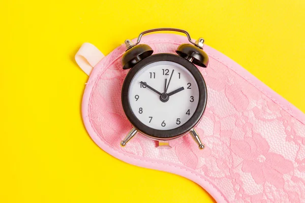 Sleeping mask and alarm clock on yellow background — Stock Photo, Image