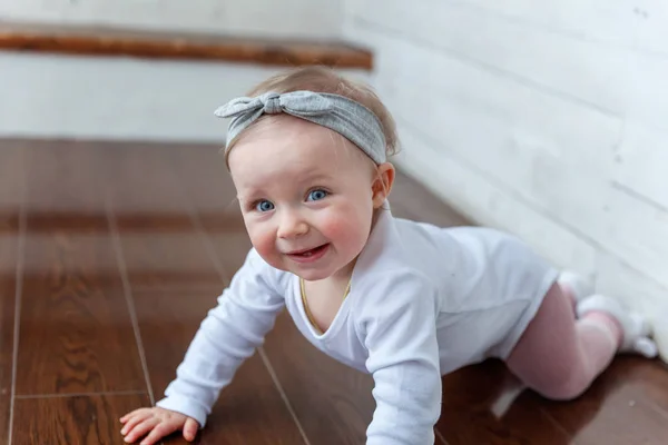 Little crawling baby girl one year old siting on floor in bright light living room near window smiling and laughing — Stock Photo, Image