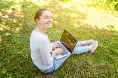Dizüstü pc bilgisayar üzerinde çalışan Şehir Parkı yeşil çim Çimenlikte oturan genç kadın. Serbest iş kavramı