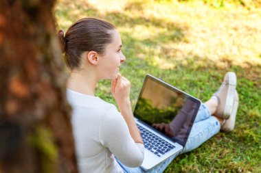 Dizüstü pc bilgisayar üzerinde çalışan Şehir Parkı yeşil çim Çimenlikte oturan genç kadın. Serbest iş kavramı