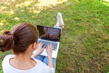 Dizüstü pc bilgisayar üzerinde çalışan Şehir Parkı yeşil çim Çimenlikte oturan genç kadın. Serbest iş kavramı