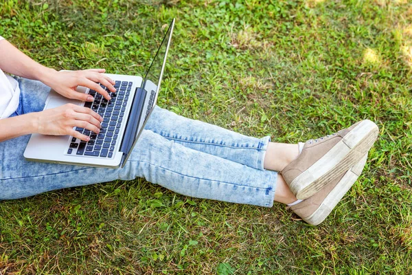 Gambe di donna sul prato erboso verde nel parco cittadino, mani che lavorano sul computer portatile pc. Concetto di impresa freelance — Foto Stock