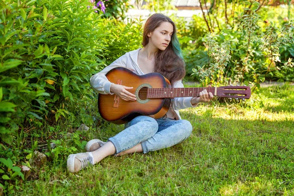 Молода жінка сидить у траві і грає на гітарі — стокове фото