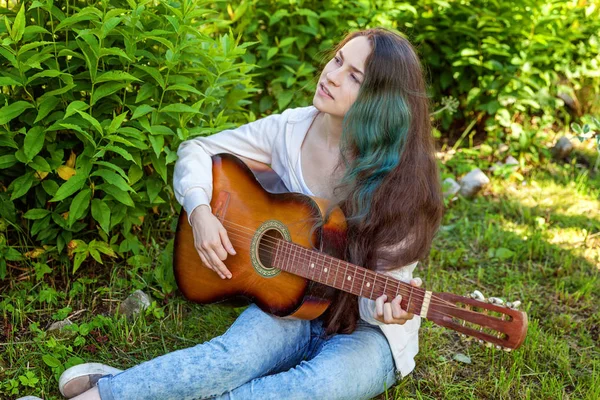 Mujer joven sentada en la hierba y tocando la guitarra —  Fotos de Stock