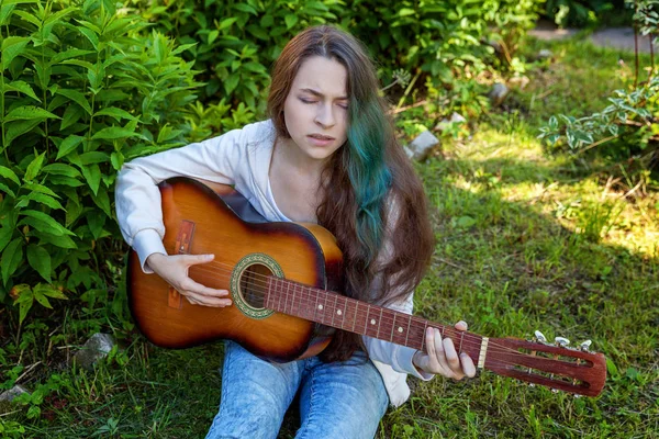 Jovem mulher sentada na grama e tocando guitarra — Fotografia de Stock