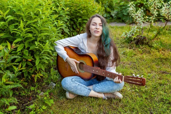 Mujer joven sentada en la hierba y tocando la guitarra —  Fotos de Stock