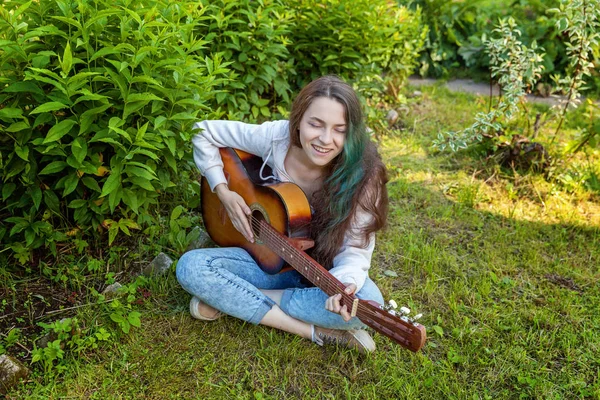 Jovem mulher sentada na grama e tocando guitarra — Fotografia de Stock