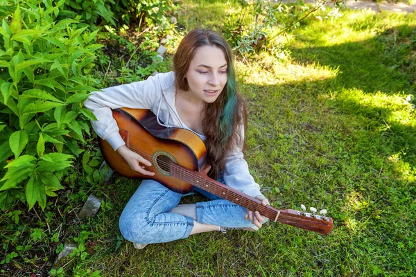 Jovem mulher sentada na grama e tocando guitarra — Fotografia de Stock