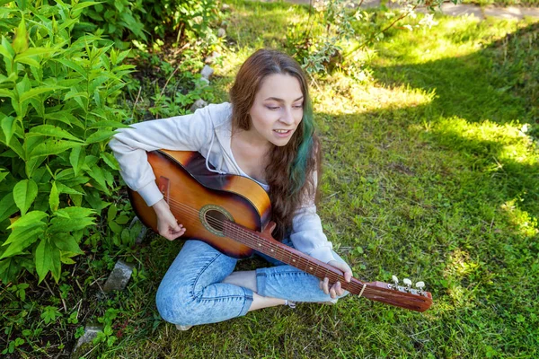 Giovane donna seduta in erba e suonare la chitarra — Foto Stock