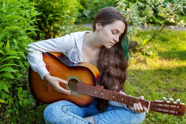 Jonge vrouw zitten in het gras en het spelen van gitaar — Stockfoto