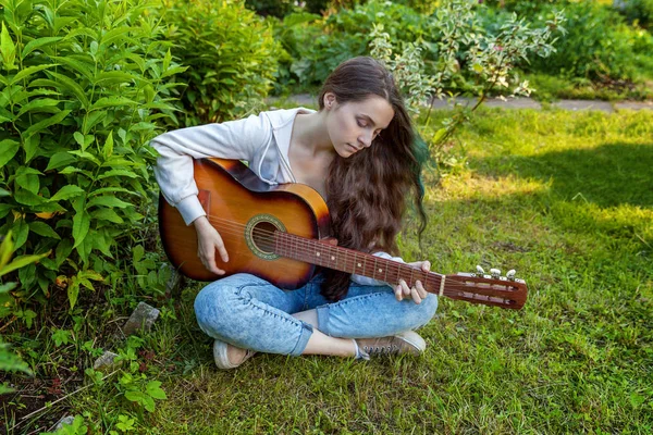 Jovem mulher sentada na grama e tocando guitarra — Fotografia de Stock