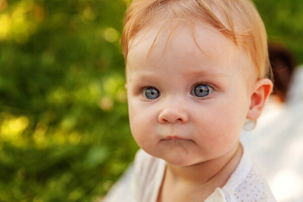 Sweet happy little baby girl sitting on grass in park, garden, meadow