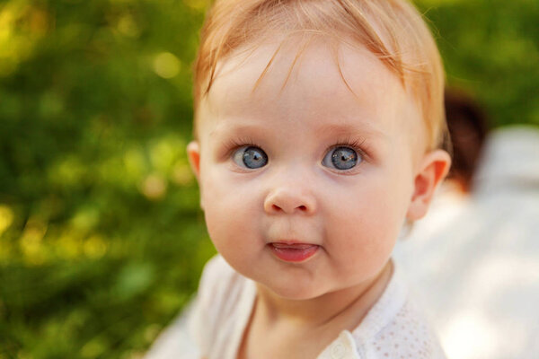 Sweet happy little baby girl sitting on grass in park, garden, meadow