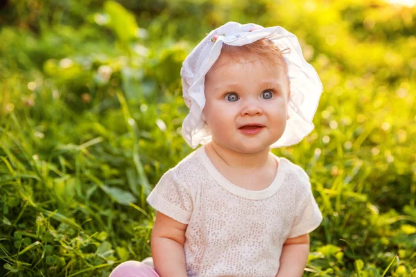 Sweet happy little baby girl sitting on grass in park, garden, meadow Stock Photo