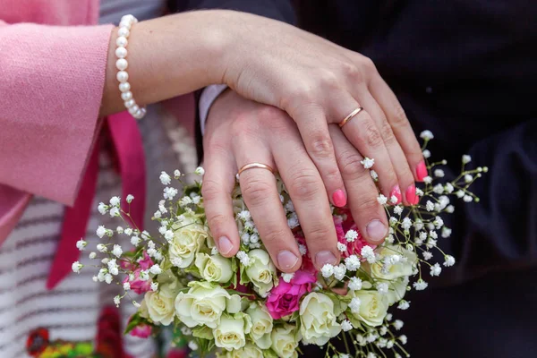 Manos de novia y novio con anillos de boda sobre fondo de ramo de flores nupciales —  Fotos de Stock
