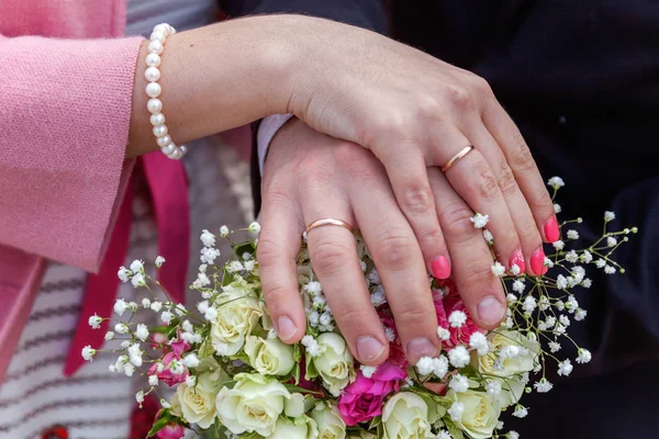 Manos de novia y novio con anillos de boda sobre fondo de ramo de flores nupciales —  Fotos de Stock