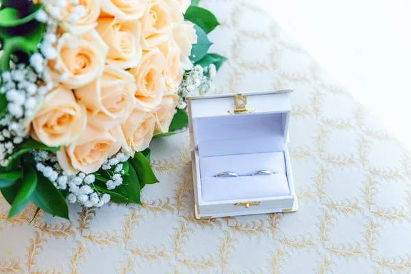 Весільні кільця лежать на світлій поверхні на тлі букета квітів — стокове фото