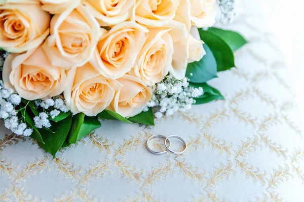 Весільні кільця лежать на світлій поверхні на тлі букета квітів — стокове фото