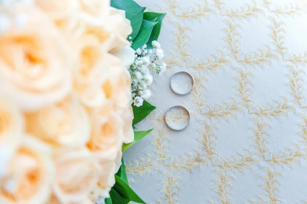 结婚戒指躺在光面上, 背景是花束 — 图库照片